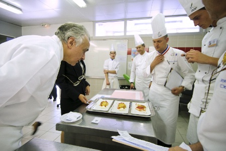 A gauche, Alain Ducasse observe attentivement les assiettes.